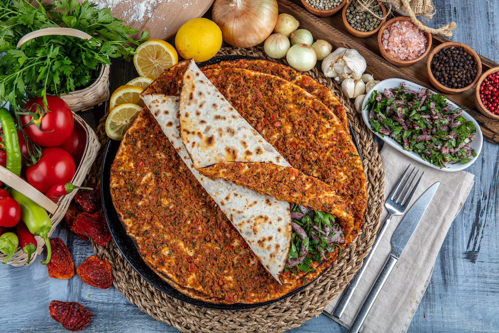 Traditional Turkish Cuisine: Lahmacun turkish delicious pizza with minced beef or lamb meat, paprika, tomatoes, cumin spice, on rustic wooden table background.