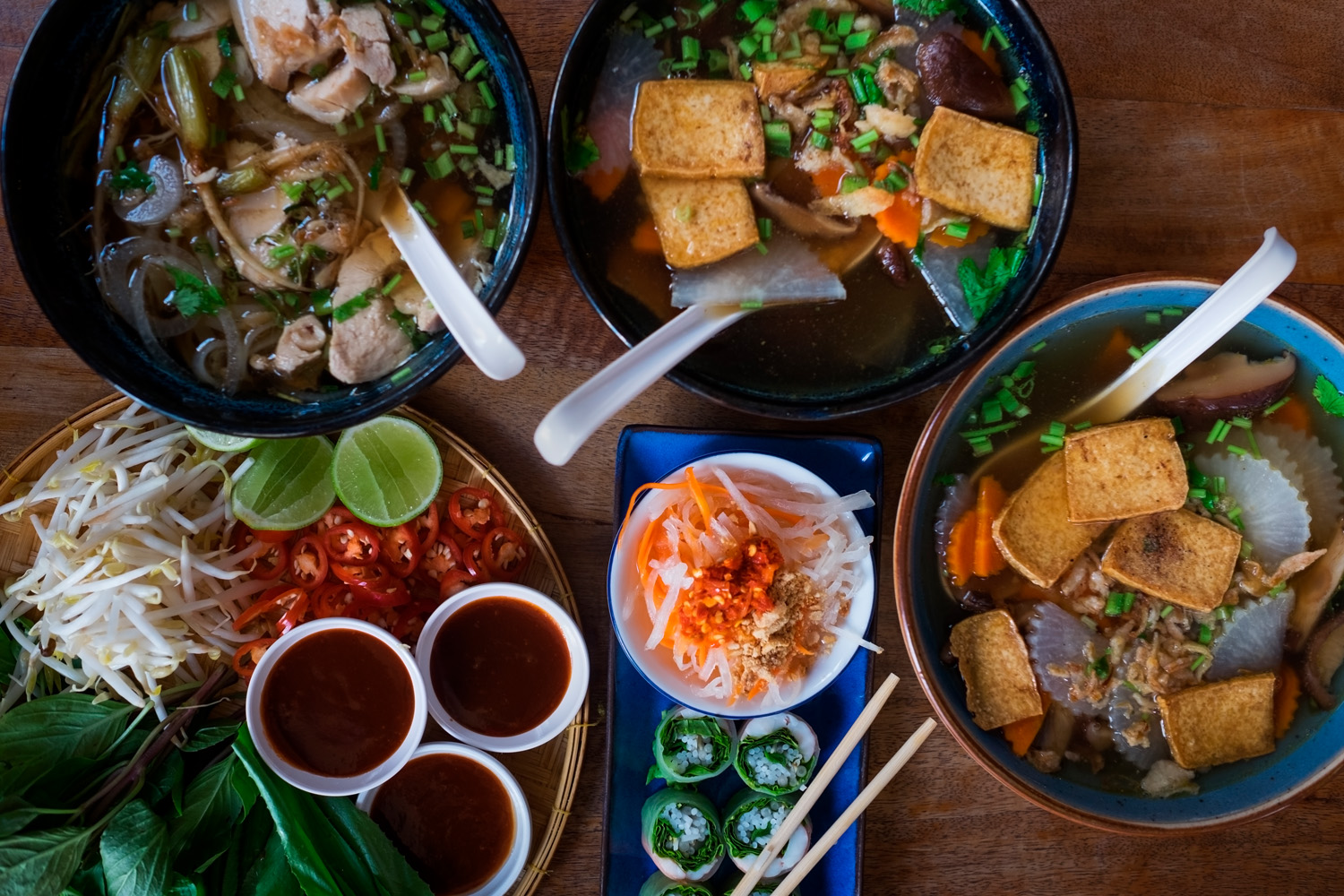 Traditional Vietnamese food. Soups, rolls and fresh herbs. Plates on a wooden surface. View from top to bottom. Vietnamese Food